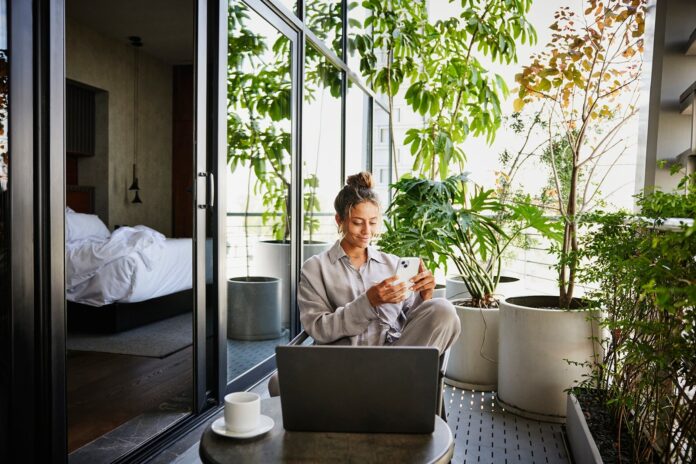 Woman-sitting-outside-hotel-patio-using-her-smart-phone-and-working-on-laptop-_Thomas-Barwick.jpg